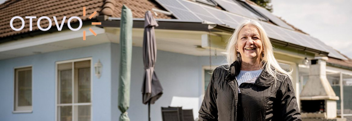 Lächelnde Person vor einem Haus mit Solaranlage